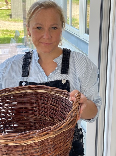 Lisa tittar in i kameran, hon har hängelsbyxor. Hon har en korg i händerna